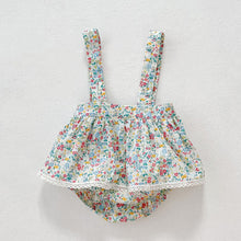 Load image into Gallery viewer, Bright floral print on a white ground with a crochet trim to the hem. Dungaree style skirt complete with popper fastenings to the crotch and button fastenings for the adjustable straps. Perfect summer outfit for baby girls. 0-6months, 6-9 months, 9-12 months, 12-18 months, 18-24 months.