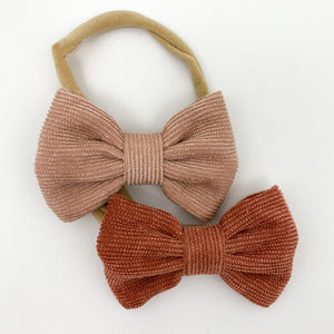 Corduroy bow headbands for baby girls, available in a variety of colours. This pack has peach and rust colours in, with a super soft and stretchy headband. Perfect to style your little ones Bel Bambini outfits with whilst looking adorably cute too. Exclusive girls headbands  at Bel Bambini baby boutique.