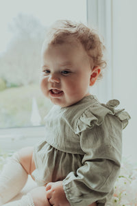 Baby girls romper exclusive to Bel Bambini. Stylish clothing for little girls. Gifts for baby and toddlers. Baby girl wearing our flutter detail romper in sage green.