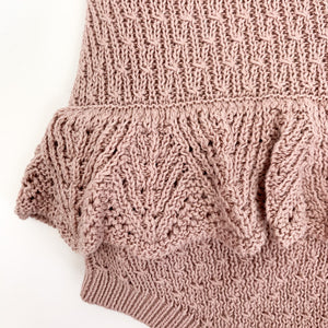 Photo showing a detail shot of our baby girls knitted romper in dusty pink. The scalloped frill to the hips make this such a beautiful style. Shop our romper collection online.